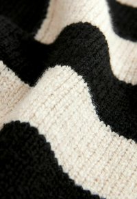 Dziane tkaniny z naprzemiennymi czarnymi i kremowymi falistymi paskami; miękka tekstura z widocznym szwem oraz puszystym, miękkim wykończeniem.