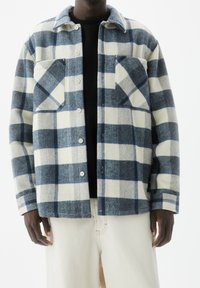 Giacca camicia a quadri blu e bianca realizzata in tessuto misto lana, con due tasche sul petto, chiusura con bottoni e colletto.