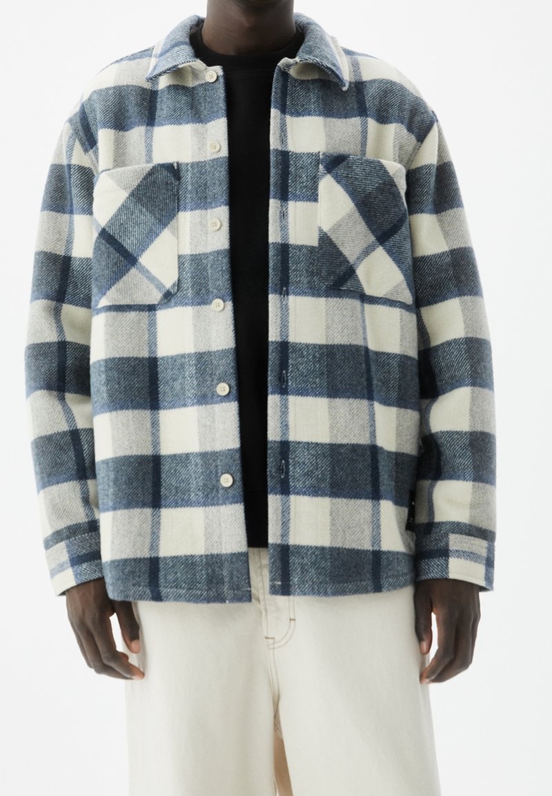 Giacca camicia a quadri blu e bianca realizzata in tessuto misto lana, con due tasche sul petto, chiusura con bottoni e colletto.