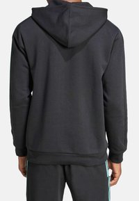 Svart hoodie med dragsko på huooden, ribbade ärmslut och fåll, samt en mjuk textur. Accentuerad med turkosa ränder på de matchande byxorna.