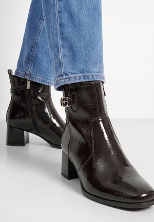 Bottines marron foncé brillantes avec talons blocs et boucles latérales portées avec un jean bleu clair.