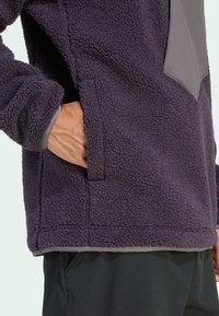 Polaire à enfiler de couleur violet profond avec une surface texturée, présentant un panneau en tissu lisse contrastant et des poches latérales.