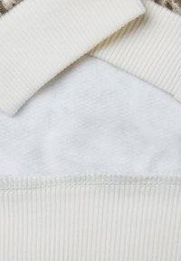 Felpa color crema con colletto e orlo a coste, caratterizzata da un interno morbido simile al pile e una superficie esterna liscia.