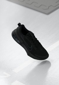Crne atletske tenisice s gornjim dijelom od mrežastog materijala i gumenim potplatom. Sadrže Nike logo i vidljivu Air Max amortizaciju. Imaju teksturiranu površinu i vezice.