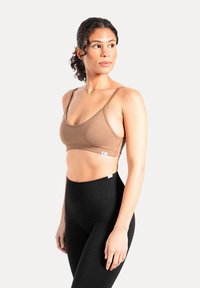 Brązowy bezszwowy biustonosz na cienkich ramiączkach, zestawiony z czarnymi legginsami o wysokim stanie. Gładka tekstura; prosty design bez zdobień.