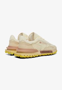 Zapatillas Lacoste de color crema con parte superior de materiales mixtos, acentos de ante, suela de goma amarilla y suela texturizada para mayor tracción.