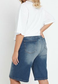 Denim-bermudashortsit, joissa on sinisen liukuvärjäyksen sävyt, takataskut, sileä pinta ja rento istuvuus. Yhdistetty valkoiseen ylisuurikokoiseen t-paitaan.