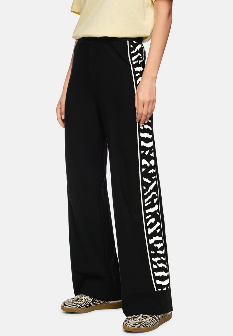Black wide-leg pants feature a white zebra stripe pattern along the outer side, made from soft cotton blend fabric.