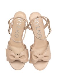 Beżowe sandały z błyszczącym akcentem w postaci kokardy, paskiem na kostkę oraz gładkim skórzanym wykończeniem; otwarty czubek i płaska podeszwa.