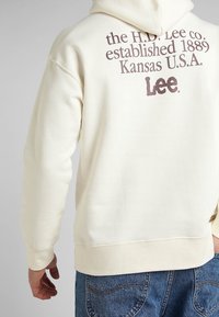 Sudadera crema hecha de un tejido suave, con un gran logo impreso y texto en la parte posterior. Corte holgado con puños y dobladillo acanalados.