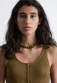 Ribbed olive tank top with buttons, paired with a green bead necklace. Features a close-up view highlighting texture and color.