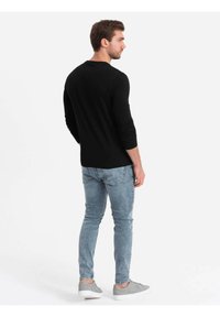 Sort langærmet skjorte, tætsiddende, sammen med lyseblå slim-fit jeans og grå sneakers. Enkel, afslappet design uden synlige logoer.