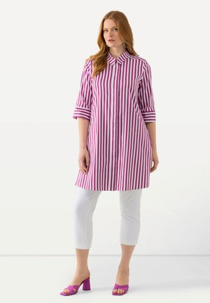 Violetin ja valkoisin raidoittein varustettu mekko, jossa on kaulus ja kolmen neljänneksen hihat; yhdistetty valkoisiin capri-housuihin ja violetteihin paksupohjaisiin sandaaleihin.