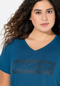 Blauwe V-hals t-shirt met een textuur graphic print in verschillende lettertypen die "POWER" en "LOVE" op de voorkant spellen.
