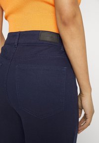 Marinblå denimjeans med slim fit, med en bakficka och kontrasterande sömmar. Texturerad midja med läderetikett.