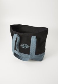 Μαύρη καμβά τσάντα tote με ανοιχτό μπλε χερούλια και κάτω μέρος. Διαθέτει ένα επιβλητικό λογότυπο στην μπροστινή πλευρά. Ανοιχτή στην κορυφή χωρίς κλείσιμο.