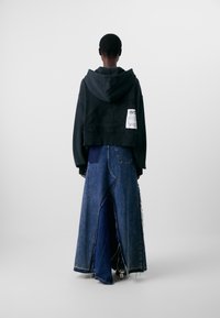 Hanorac negru scurt cu o glugă mare, combinat cu o fustă lungă, asimetrică din denim. Fusta are nuanțe mixte de denim și margini desfăcute.