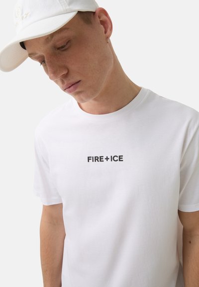 Bílý bavlněný tričko s krátkým rukávem, na kterém se uprostřed hrudi nachází černé logo "FIRE+ICE", nošené pod bílou kšiltovkou. Hladký povrch.