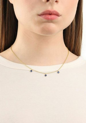 Collana in oro con tre gemme blu equidistanti lungo la lunghezza, su un top chiaro a coste.