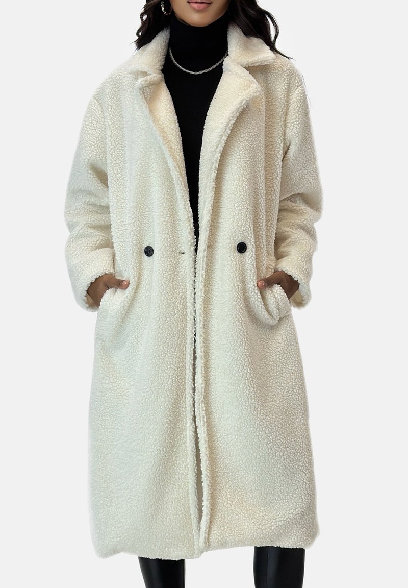 Roomkleurige, oversized jas gemaakt van zachte, gestructureerde stof. Heeft een kraag, twee voorszakken en dubbele zwarte knopen.