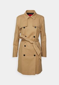 Trench-coat beige double boutonnage avec des boutons noirs, une ceinture à la taille nouée à l'avant, des manches longues et un col classique.