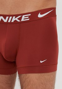Boxeri Nike roșii, cu un tiv elastic alb pe care este inscripționat logo-ul Nike, cu o textură netedă și un design ajustat pentru confort.