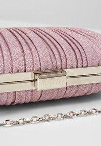 Rosa glittrande clutch med plisserad tygdesign, guldfärgad hårdvara, graverad stängning och en silverkedjespänne. Texturerad yta.