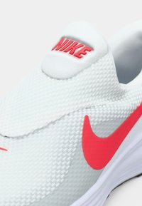 Nike slip-on αθλητικά παπούτσια, με ελαφρύ γκρι διχτυωτό επάνω μέρος, κόκκινη λογότυπο λεπτομέρεια, ομαλό εσωτερικό και λευκή σόλα. Υφή επιφάνειας.