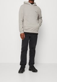 Hellgrauer Hoodie mit Kängurutasche, gerippten Bündchen und Saum. Kombiniert mit dunkler Hose und schwarzen Sneakers mit schlankem Design.