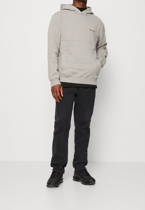 Sudadera con capucha gris claro con bolsillo canguro, puños y dobladillo acanalados. Combinada con pantalones oscuros y zapatillas negras, con un diseño elegante.