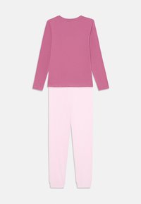 Långärmad topp i rosa, tillsammans med matchande rosa pyjamasbyxor. Tyget har en mjuk textur; ensemblet har en enkel, minimalistisk design.