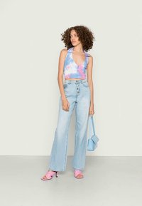 Top cortado em tie-dye nas cores rosa pastel e azul, calças de ganga flared de lavagem clara e de cintura alta, saltos quadrados rosa e uma pequena mala azul.
