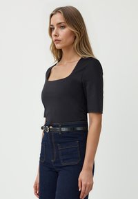 Zwarte top met korte mouwen en een vierkante halslijn, gemaakt van soepele stof, gecombineerd met high-waisted donkere spijkerbroek met contrasterende stiksels.