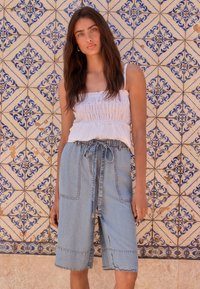Top bianco senza maniche con texture arricciata e dettagli traforati, abbinato a culottes in denim blu con tasche e vita con coulisse.