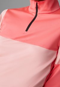 Quarter-zip tröja i korall och ljusrosa, med en mjuk och lätt tyg, med svart dragkedja och detaljer på kragen.