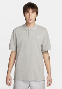 Világosszürke pólóing, puha anyagból készült, hajtott gallérral, rövid ujjú, három gombbal és egy kis fehér Nike logóval a mellen.