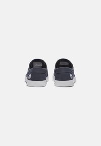 Marineblaue Canvas-Slipper mit weißen Gummisohlen, die ein Logo an der Ferse und eine strukturierte Oberseite für besseren Grip aufweisen.
