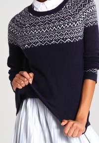 Dunkelblaues Sweatshirt aus weichem Material. Mit einem weißen geometrischen Muster am Hals und dezenten Verzierungen. Lockerer Schnitt, gerippte Bündchen.