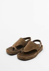 Sandales en suède marron avec une boucle pour les orteils et un design ajouré, dotées d'une sangle ajustable et d'une semelle plate.