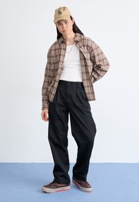 Brun rutigt knapp-up skjorta, vit linne, svarta skräddarsydda byxor, bruna skor med röd yttersula. Avslappnad outfit med lager av texturer.