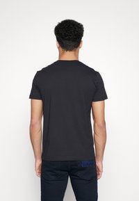 Musta puuvillapaita, jossa on pyöreä kaula-aukko, lyhyet hihat ja yksinkertainen selkä. Pohjassa on huomaamaton sininen logo.