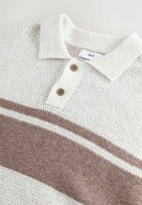Texturiertes weißes Sweatshirt mit einem hellbraunen horizontalen Streifen und einem Kragen mit zwei Knöpfen. Hergestellt aus gestricktem Stoff, bietet eine lockere Passform.