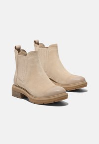 Beige Wildleder-Stiefeletten mit elastischen Seitenpaneelen, runder Spitze und einer strukturierten Gummisohle. Sie verfügen über einen niedrigen Blockabsatz für Stabilität.