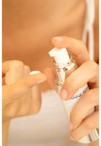 White pump bottle with a silver accent, dispensing a small amount of cream onto a fingertip. Smooth texture and sleek design.