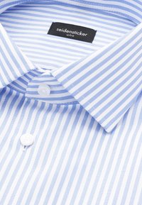 Chemise à rayures bleues et blanches avec boutons blancs et une étiquette noire indiquant « seidensticker uno » à l’intérieur du col.