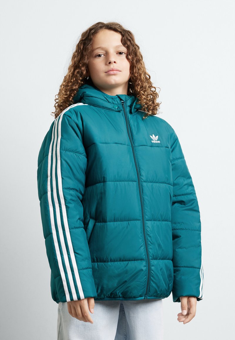 Zilā pūkaina jaka ar kapuci, ar baltām svītrām uz piedurknēm, ar rāvējslēdzēju un quilted tekstūru. Adidas logo uz krūtīm.