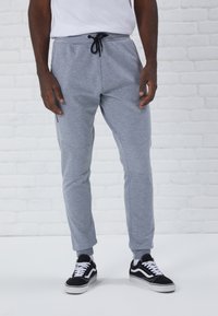 Gray jogger pants made of soft fabric, featuring a drawstring waist, tapered legs, side pockets, and ribbed cuffs. Worn with black sneakers.
