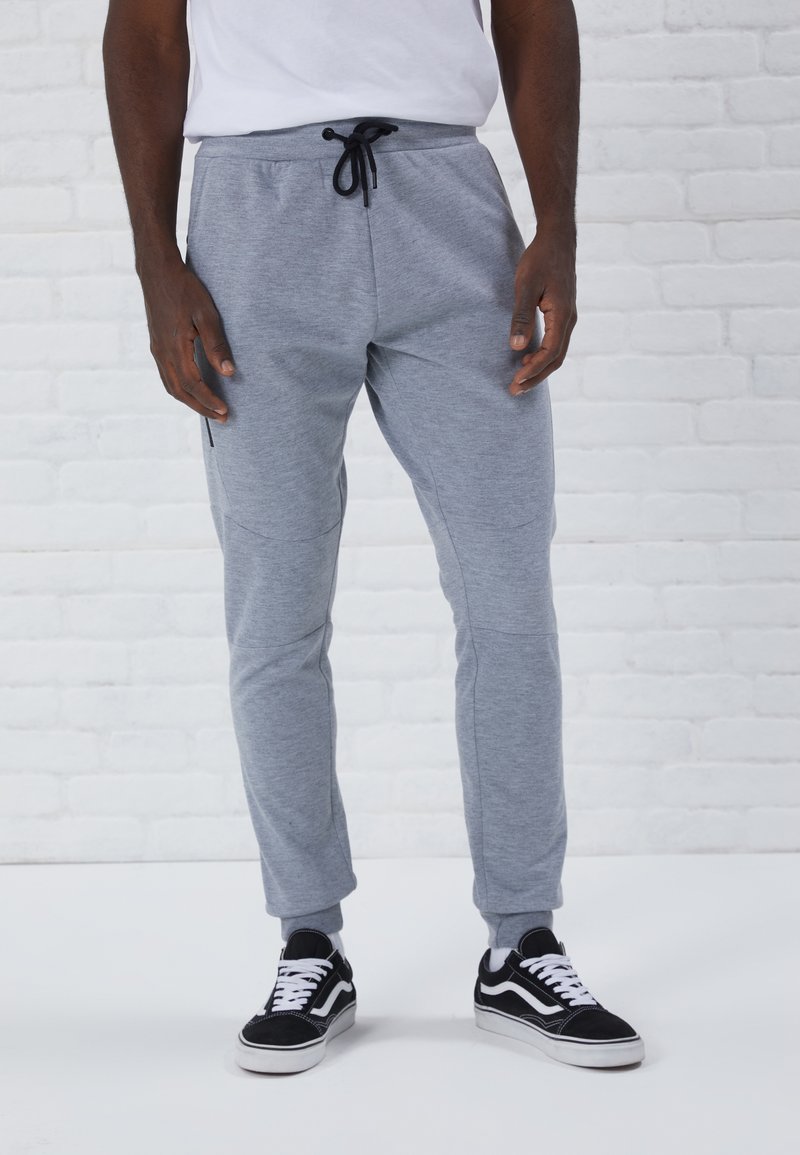 Gray jogger pants made of soft fabric, featuring a drawstring waist, tapered legs, side pockets, and ribbed cuffs. Worn with black sneakers.