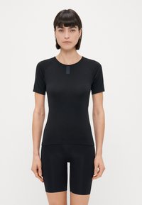 Zwart T-shirt met korte mouwen, ronde hals en raglanmouwen. Soepele textuur met een klein label bij de kraag. Gdragen met een zwarte short.