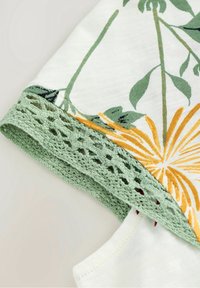Hvid bomulds skjorte med grøn blomsterprint, gule detaljer og en struktureret grøn hæklede kant langs kanten.